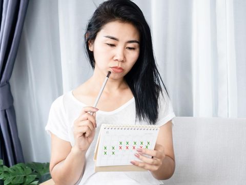 Asian woman having problem with amenorrhea, irregular periods and counting her menstrual cycles on calendar