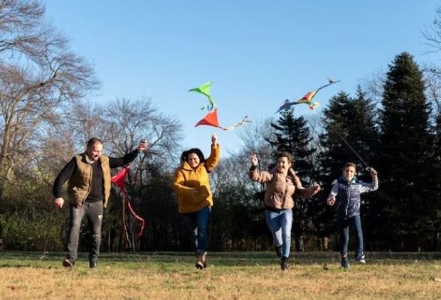Melakukan hal menyenangkan/ foto: Freepik/ freepik Empat orang berlarian menerbangkan layangan