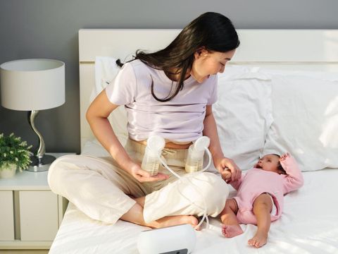 happy mother using breast pump machine to pumping milk while talking with her newborn baby on a bed