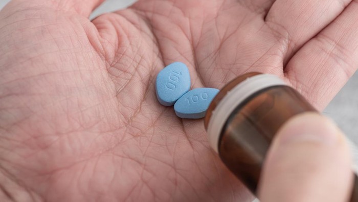 Man hold blue pill viagra in fingers on blue background. Medicine concept of men health, medication for potency, erection, treatment of erectile dysfunction Macro shot