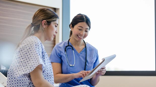 At the hospital, the mid adult female doctor gives her young adult female patient the good news from her medical tests.