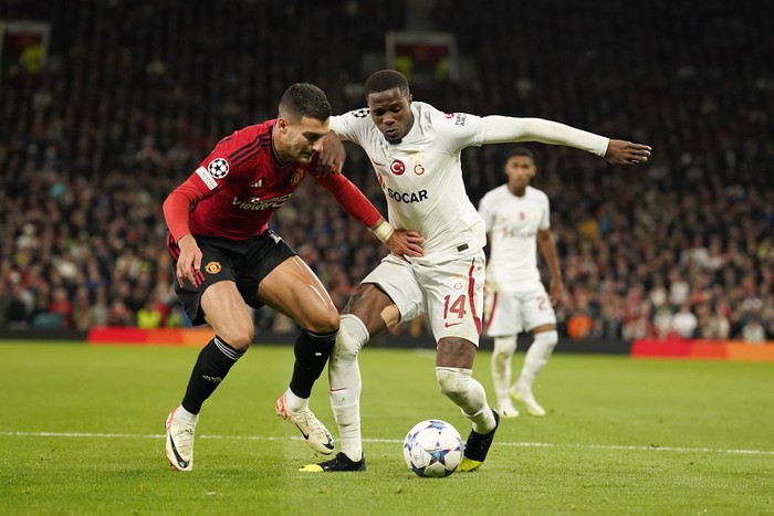 Manchester United's Diogo Dalot, left, challenges for the ball with Galatasaray's Wilfried Zaha during the Champions League group A soccer match between Manchester United and Galatasaray at the Old Trafford stadium in Manchester, England, Tuesday, Oct. 3, 2023. (AP Photo/Dave Thompson)