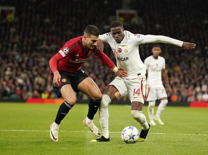 Manchester United's Diogo Dalot, left, challenges for the ball with Galatasaray's Wilfried Zaha during the Champions League group A soccer match between Manchester United and Galatasaray at the Old Trafford stadium in Manchester, England, Tuesday, Oct. 3, 2023. (AP Photo/Dave Thompson)