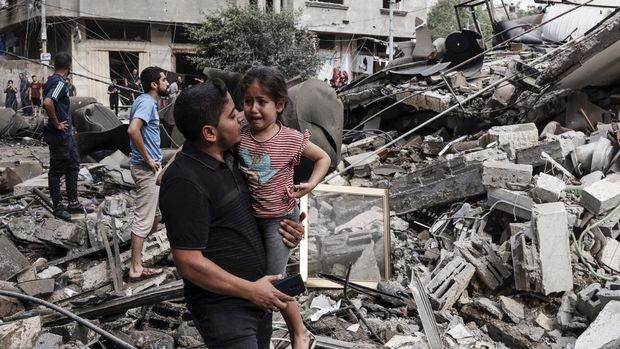 EDITORS NOTE: Graphic content / A man carries a crying child as he walks in front of a building destroyed in an Israeli air strike in Gaza City on October 7, 2023. Palestinian militants have begun a 