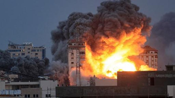PALESTINIAN-ISRAEL-GAZA-CONFLICT EDITORS NOTE: Graphic content / People standing on a rooftop watch as a ball of fire and smoke rises above a building in Gaza City on October 7, 2023 during an Israeli air strike that hit the Palestine Tower building. At least 70 people were reported killed in Israel, while Gaza authorities released a death toll of 198 in the bloodiest escalation in the wider conflict since May 2021, with hundreds more wounded on both sides. (Photo by MAHMUD HAMS / AFP)