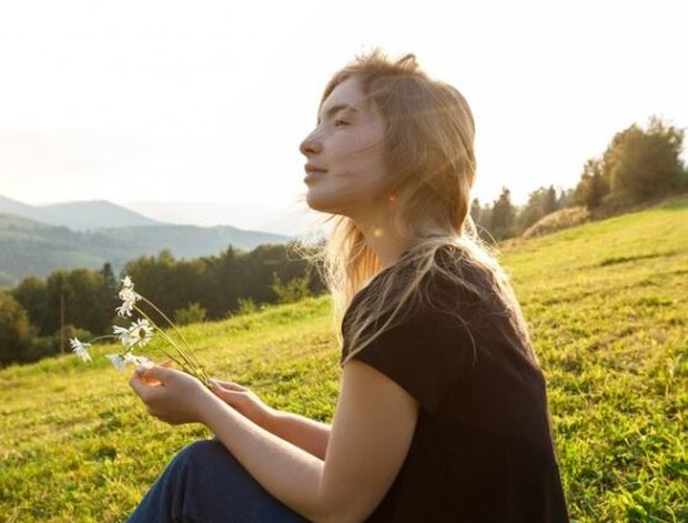 Perempuan duduk di padang bunga sambil menatap ke depan
