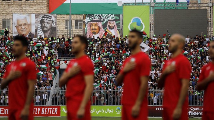 The Palestinian national football team stand for their national anthem during a World Cup 2022 Asian qualifying match between Palestine and Saudi Arabia in the Israeli occupied West Bank town of al-Ram on October 15, 2019. Portraits of Saudi King Salman, Saudi Crown Prince Mohamed bin Salman, late Palestinian leader Yasser Arafat and current Palestinian leader Mahmud Abbas. The game would mark a change in policy for Saudi Arabia, which has previously played matches against Palestine in third countries. Arab clubs and national teams have historically refused to play in the West Bank, where the Palestinian national team plays, as it required them to apply for Israeli entry permits. (Photo by Ahmad GHARABLI / AFP)