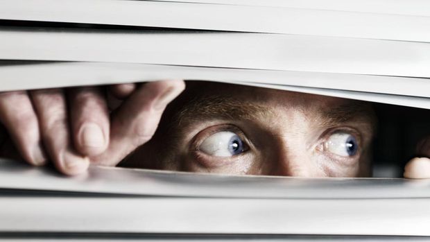 This terrified man looking out to the side  through a venetian blind could be witnessing a crime, watching the suspicious behavior of neighbors, or simply a paranoid, isolated shut-in.