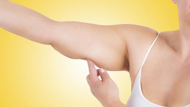 Healthcare and medicine: close up view of unrecognizable woman pointing her arm showing fat excess and flabby skin shot against yellow background. High resolution 42Mp studio digital capture taken with Sony A7rII and Sony FE 90mm f2.8 macro G OSS lens