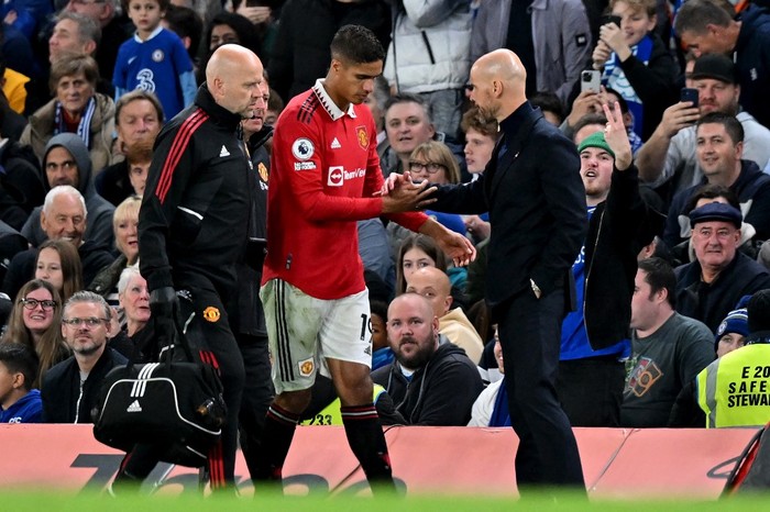 Manchester Uniteds French defender Raphael Varane (C) is consoled by Manchester Uniteds Dutch manager Erik ten Hag (R) as he leaves the pitch after picking up an injury during the English Premier League football match between Chelsea and Manchester United at Stamford Bridge in London on October 22, 2022. (Photo by Glyn KIRK / IKIMAGES / AFP) / RESTRICTED TO EDITORIAL USE. No use with unauthorized audio, video, data, fixture lists, club/league logos or live services. Online in-match use limited to 45 images, no video emulation. No use in betting, games or single club/league/player publications. /