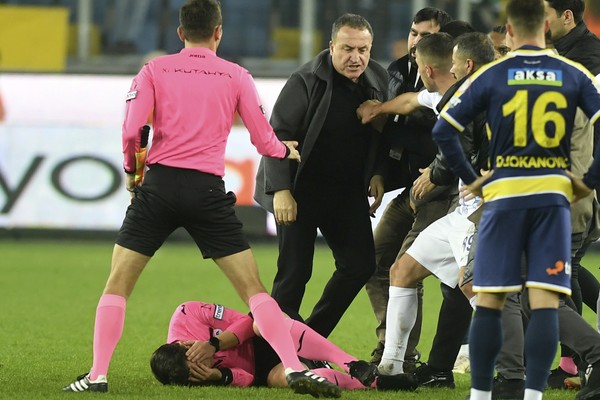 Referee Halil Umut Meler holds his face as he lies on the ground after being punched by MKE Ankaragucu president Faruk Koca, center, at the end of the Turkish Super Lig soccer match between MKE Ankaragucu and Caykur Rizespor in Ankara, Monday, Dec. 11, 2023. The Turkish Football Federation has suspended all league games in the country after a club president punched the referee in the face at the end of a top-flight match. Koca was arrested Tuesday, Dec. 12, 2023, along with two other people on charges of injuring a public official following questioning by prosecutors.  (Abdurrahman Antakyali/Depo Photos via AP)