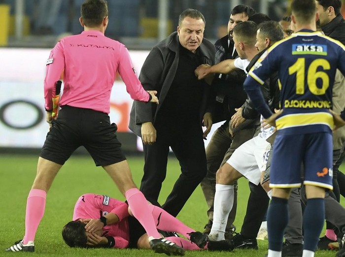 Referee Halil Umut Meler holds his face as he lies on the ground after being punched by MKE Ankaragucu president Faruk Koca, center, at the end of the Turkish Super Lig soccer match between MKE Ankaragucu and Caykur Rizespor in Ankara, Monday, Dec. 11, 2023. The Turkish Football Federation has suspended all league games in the country after a club president punched the referee in the face at the end of a top-flight match. Koca was arrested Tuesday, Dec. 12, 2023, along with two other people on charges of injuring a public official following questioning by prosecutors.  (Abdurrahman Antakyali/Depo Photos via AP)