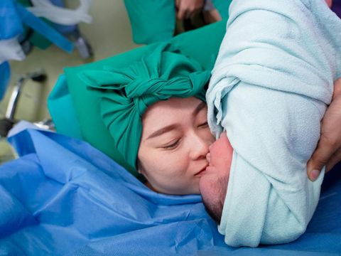 Newborn baby in delivery room.Blurred Mother background giving birth to a baby and kiss her baby. Woman pregnant patient in a hospital. Parent and infant first moments of bonding.