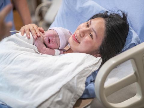 Newborn baby in delivery room.Blurred Mother background giving birth to a baby and kiss her baby. Woman pregnant patient in a hospital. Parent and infant first moments of bonding.