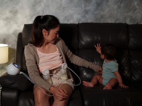 mother using breast pump machine to pumping milk with infant baby on a sofa in the living room at night