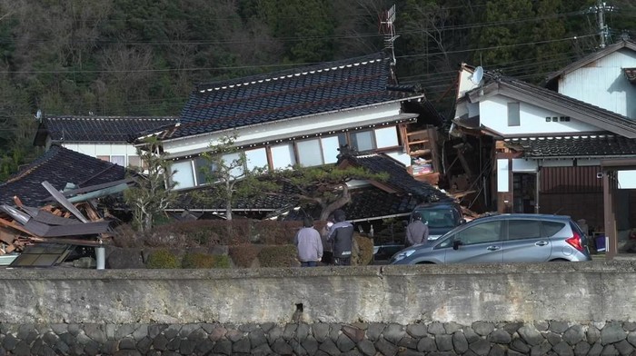 This screen grab from AFPTV video footage taken on January 2, 2024 shows people looking at damage to a house in Wajima, Ishikawa prefecture, a day after a major 7.5 magnitude earthquake struck the Noto region in Ishikawa prefecture. Japanese rescuers battled against the clock and powerful aftershocks on January 2 to find survivors of a major earthquake that struck on New Years Day, killing at least six people and leaving a trail of destruction. (Photo by Fred Mery / AFPTV / AFP)