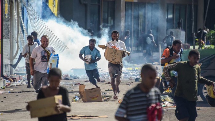 People run with merchandise as crowds leave shops with looted goods amid a state of unrest in Port Moresby on January 10, 2024. A festering pay dispute involving Papua New Guineas security forces on January 10 sparked angry protests in the capital, where a crowd torched a police car outside the prime ministers office. By Wednesday afternoon pockets of unrest had spread through the capital Port Moresby, with video clips on social media showing crowds looting shops and stretched police scrambling to restore order. (Photo by Andrew KUTAN / AFP)