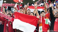 Suporter meneriakkan yel-yel dukungan sambil membentangkan bendera merah putih dan syal.
