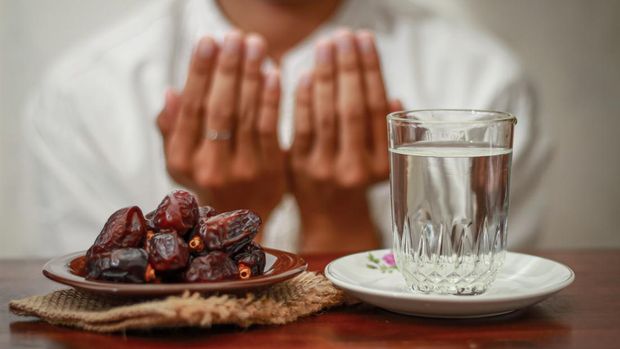 Fast breaking meal or iftar dish with muslim man hands praying to Allah. Dates with a glass of mineral water on the table.Traditional Ramadan, fast breaking meal. Ramadan kareem fasting month concept.