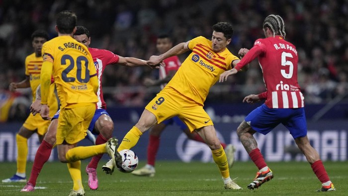 Barcelonas Robert Lewandowski, center, fights for the ball with Atletico Madrids Rodrigo De Paul, right, and Atletico Madrids Stefan Savic during the La Liga soccer match between Atletico Madrid and Barcelona at the Metropolitano stadium in Madrid, Spain, Sunday, March 17, 2024. (AP Photo/Bernat Armangue)