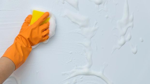 Woman hand cleaning blue wall with sponge.