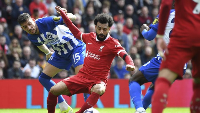 Brightons Jakub Moder, left, challenges for the ball with Liverpools Mohamed Salah, centre, during the English Premier League soccer match between Liverpool and Brighton and Hove at Anfield Stadium in Liverpool, England, Sunday, March 31, 2024. (AP Photo/Rui Vieira)