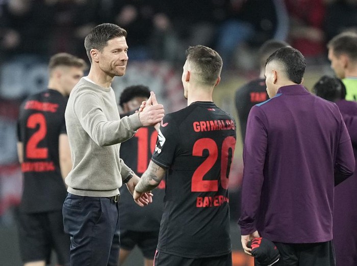 Leverkusen's head coach Xabi Alonso, centre left, celebrates with Leverkusen's Alex Grimaldo after the Europa League quarterfinals first leg soccer match between Bayer 04 Leverkusen and West Ham United at the BayArena in Leverkusen, Germany, Thursday, April 11, 2024. (AP Photo/Martin Meissner)