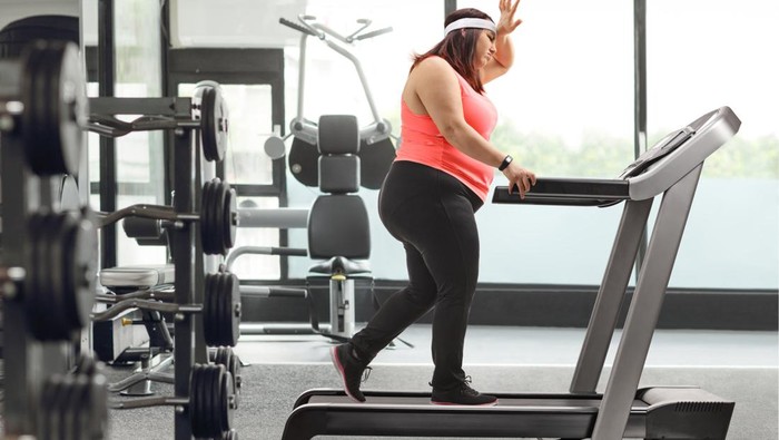 1905836391 Tired woman exercising on a treadmill and holding her forhead at a gym