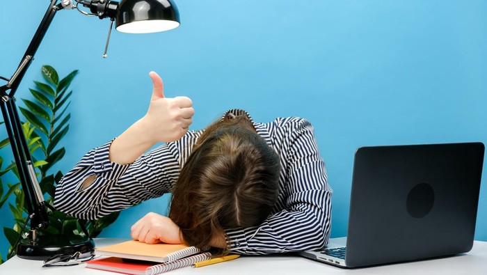 Tired exhausted secretary employee business woman in shirt sitting work sleep laid her head down on office desk with pc laptop show thumb up gesture, isolated on blue color background wall in studio