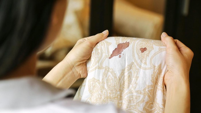Women hold bed sheet with period blood spot stains on blur background. Need to be cleaning.
