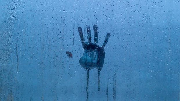 Palm print on foggy glass with water drops. Background is deep blue and gives gloomy impression