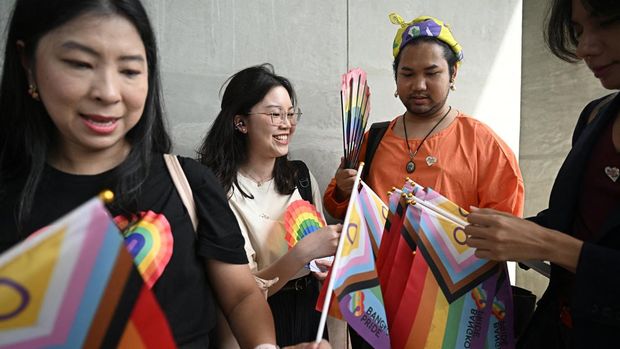 Members of the LGBTQ community pass out rainbow flags outside Parliament ahead of the final senatorial vote on the same-sex marriage bill in Bangkok on June 18, 2024. Thai lawmakers met on June 18 to vote on legalising same-sex marriage, putting the kingdom on the cusp of becoming the first Southeast Asian nation to recognise marriage equality. (Photo by Lillian SUWANRUMPHA / AFP)