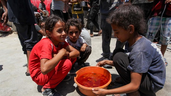 Duka Anak Palestina yang Kekurangan Makanan Children look on as Palestinians gather to receive food cooked by a charity kitchen, amid shortages of aid supplies, as the conflict between Israel and Hamas continues, in Khan Younis, in the southern Gaza Strip, June 19, 2024. REUTERS/Hatem Khaled