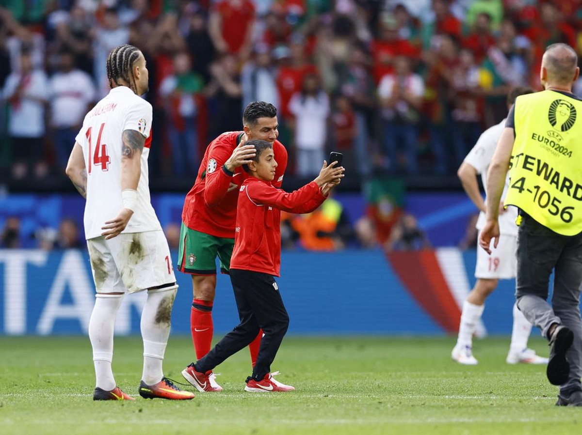 Cristiano Ronaldo diajak berselfie oleh suporter cilik di atas lapangan, Roberto Martinez menaruh perhatian. (Foto: REUTERS/Leon Kuegeler)