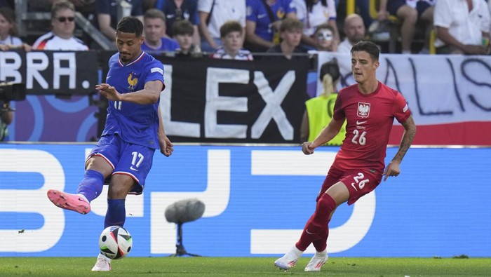 William Saliba of France, left, crosses the ball in front of Polands Kacper Urbanski during a Group D match between France and Poland at the Euro 2024 soccer tournament in Dortmund, Germany, Tuesday, June 25, 2024. (AP Photo/Hassan Ammar)
