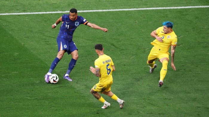 MUNICH, GERMANY - JULY 02: Cody Gakpo of the Netherlands scores his teams first goal whilst under pressure from Marius Marin and Andrei Ratiu of Romania during the UEFA EURO 2024 round of 16 match between Romania and Netherlands at Munich Football Arena on July 02, 2024 in Munich, Germany. (Photo by Alexander Hassenstein/Getty Images)