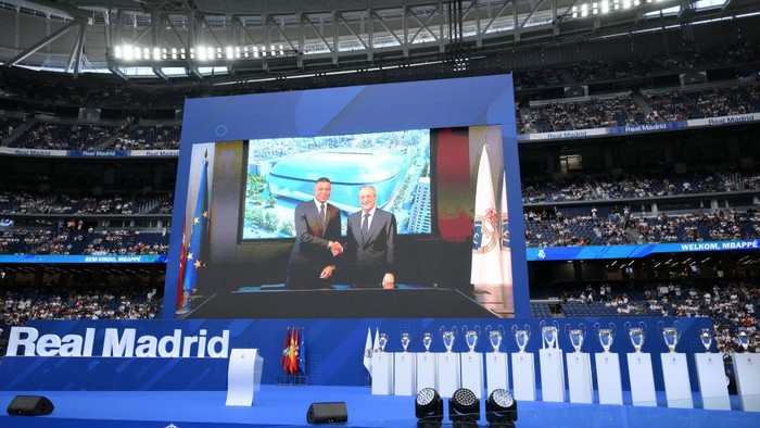 Kylian Mbappe MADRID, SPAIN - JULY 16: The big screen shows an image of Kylian Mbappe shaking hands with Florentino Perez Rodriguez, President of Real Madrid as Real Madrid new signing, Kylian Mbappe is unveiled at Estadio Santiago Bernabeu on July 16, 2024 in Madrid, Spain. (Photo by David Ramos/Getty Images)