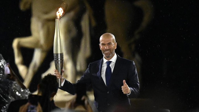 France soccer star Zinedine Zidane holds the Olympic flame on stage at the Trocadero during the opening ceremony for the 2024 Summer Olympics in Paris, France, Friday, July 26, 2024. (Loic Venance/Pool Photo via AP)