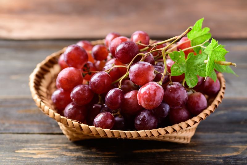 Fresh red grapes fruit in a basket on wooden background