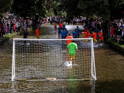 Dua tim yang beranggotakan enam orang memainkan pertandingan sepak bola di air sungai yang dangkal.