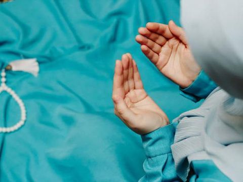 Muslim woman in a headscarf praying and a prayer beads in the background