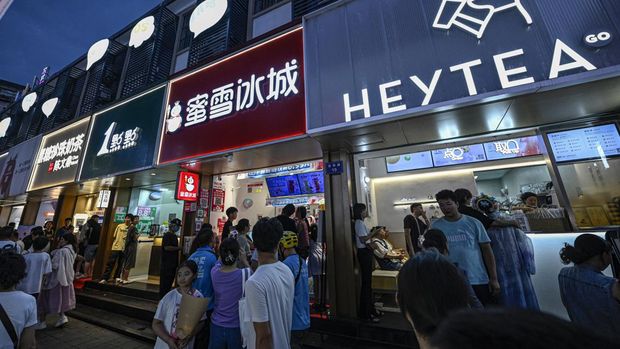 This photo taken on August 15, 2024 shows people walking past bubble tea shops at a night market in Hangzhou, in eastern China's Zhejiang province. Sweet, milky and colourful -- bubble tea is wildly popular in China, where people sipping through straws from large plastic cups is a common sight in high streets and shopping malls across the country. (Photo by Jade GAO / AFP) / To go with 'CHINA-ECONOMY-YOUTH-CONSUMERS, FOCUS' by Peter Catterall with Isabel Kua in Beijing