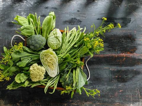 Market fresh green leaf vegetables in an old wooden crate on an old wooden table. Vegetables include, broccoli, cauliflower, cabbage, spring greens, bok choy, spinach and choy sum.