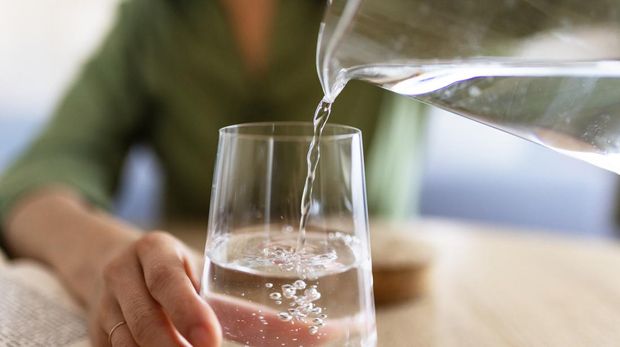 Close Up of Woman Pouring Water From Jug Into Glass