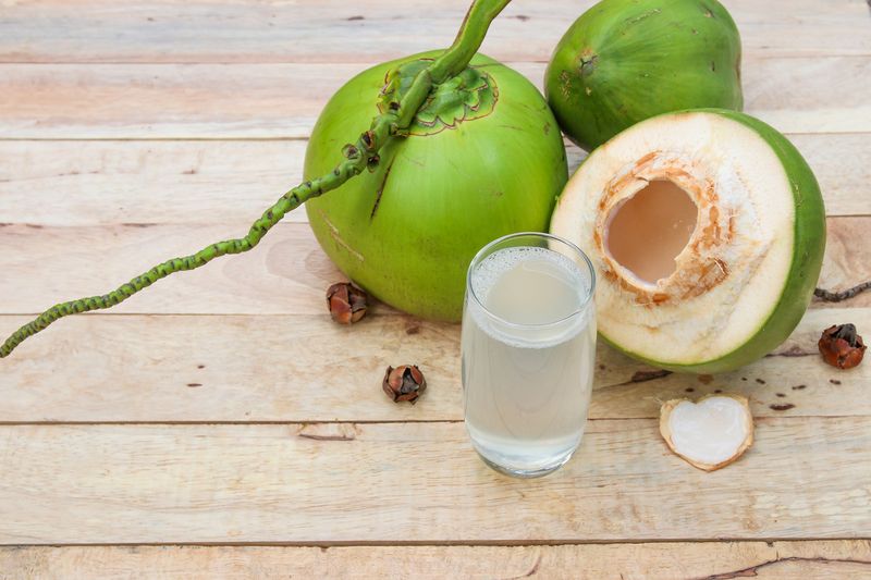 Ilustrasi air kelapa Fresh Coconut Water Drink in glass with coconut leaf on wooden background