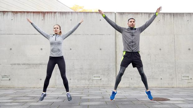 fitness, sport, people, exercising and lifestyle concept - happy man and woman doing jumping jack or star jump exercise outdoors