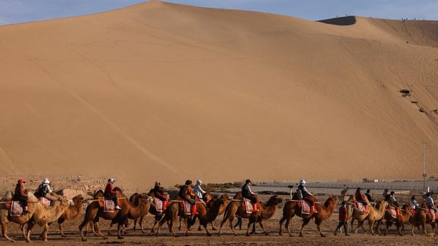 Tourists ride on camels as they visit Mingsha Mountain, during an organised media tour to Dunhuang, in Gansu province, China October 15, 2024. REUTERS/Tingshu Wang