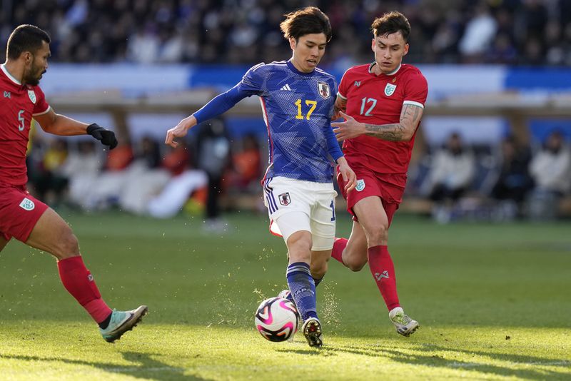 Ao Tanaka, center, of Japan, tries to score a goal against Look Saa Nicholas Kengkhetkid Mickelson Rungrat Phumichantuk, right, of Thailand during a friendly soccer match in Tokyo, Japan, Monday, Jan. 1, 2024.(AP Photo/Shuji Kajiyama)