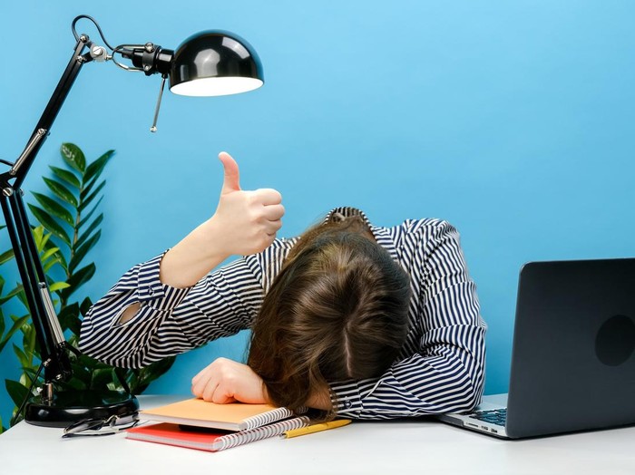 Jam Koma Gen Z Tired exhausted secretary employee business woman in shirt sitting work sleep laid her head down on office desk with pc laptop show thumb up gesture, isolated on blue color background wall in studio