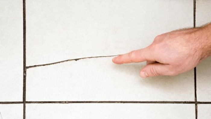 Ilustrasi ubin/lantai keramik kamar mandi retak. Mans hand finger pointing to the cracked tile on the floor. Building problems and solutions concept.